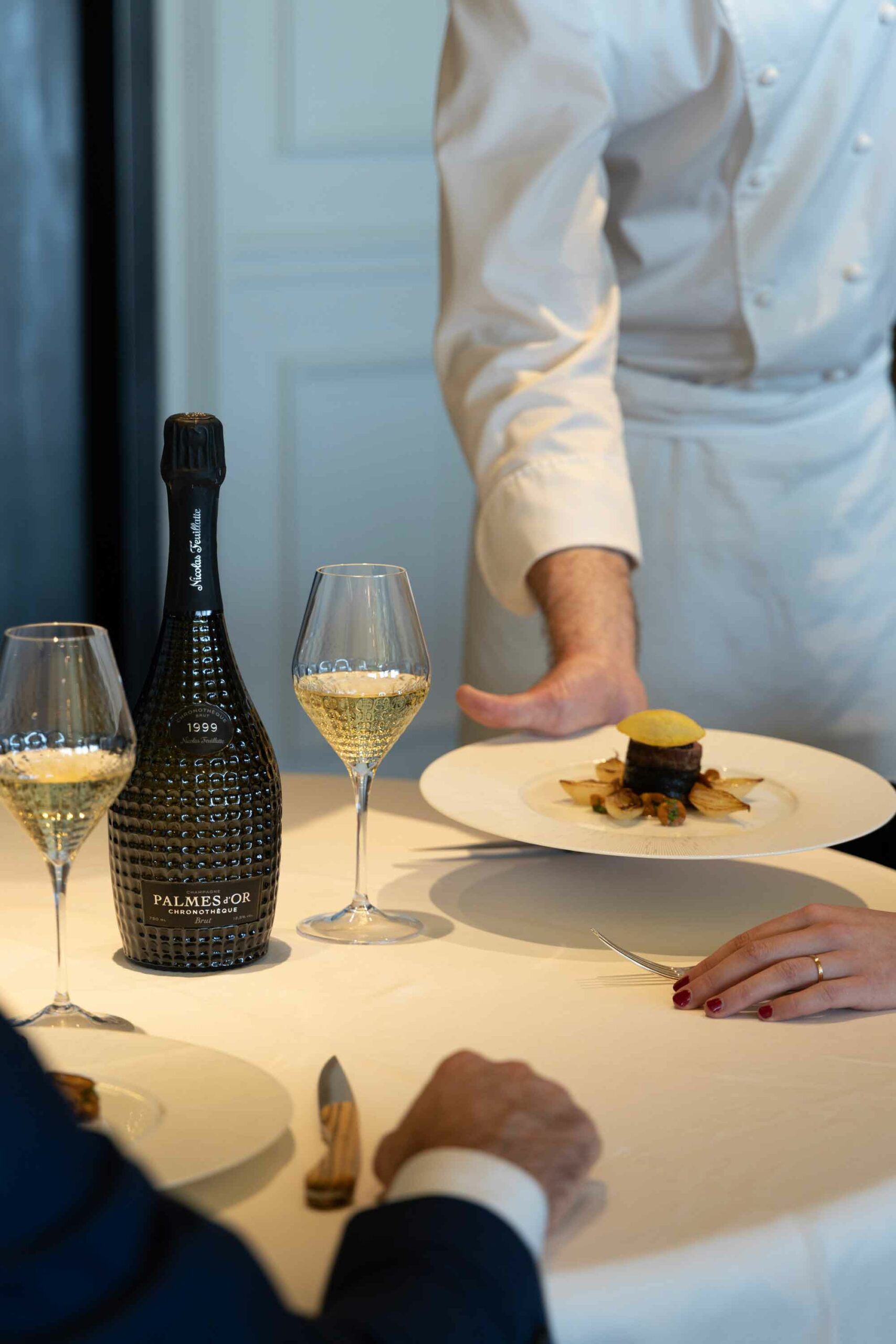 Le Chef du restaurant étoilé du Royal Champagne pose une assiette sur la table à côté de la Cuvée Chronothèque Palmes d'Or Champagne Nicolas Feuillatte | Réalisation Agence de communication Discovery